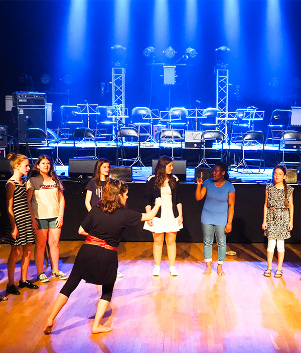 Eva Arnaud anime l’atelier EchoNova – Chœur des musiques en mouvement, un groupe de participants chante et explore la musique en mouvement sur scène, mêlant voix et expression corporelle.